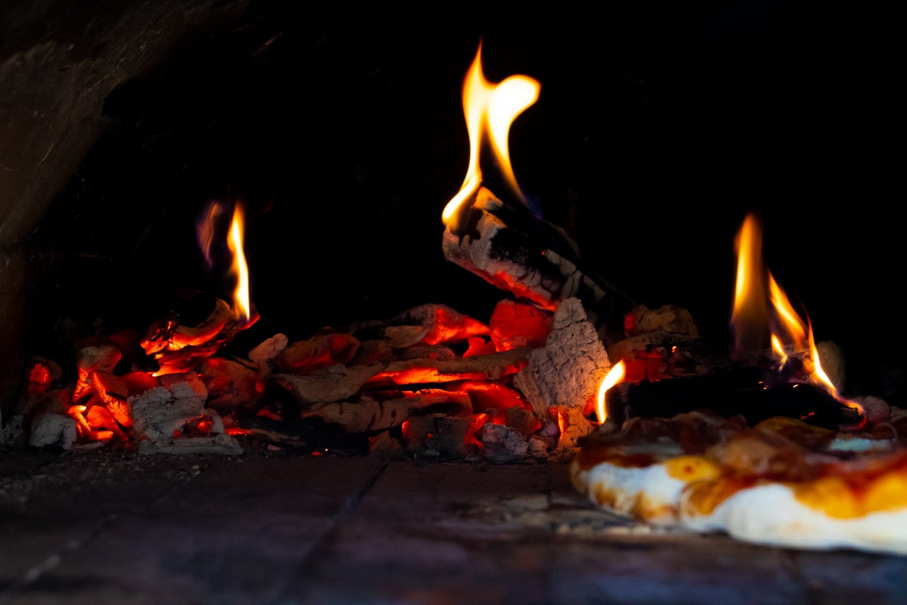Charcoal and flame inside the mouth of a pizza oven