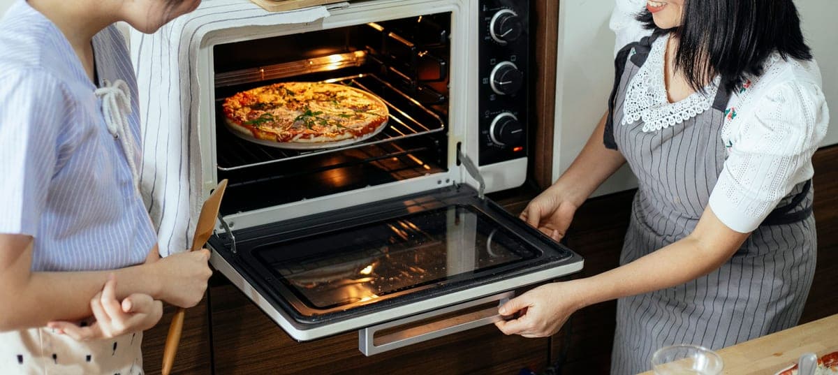 An electric countertop pizza oven in a domestic kitchen with a pizza going in