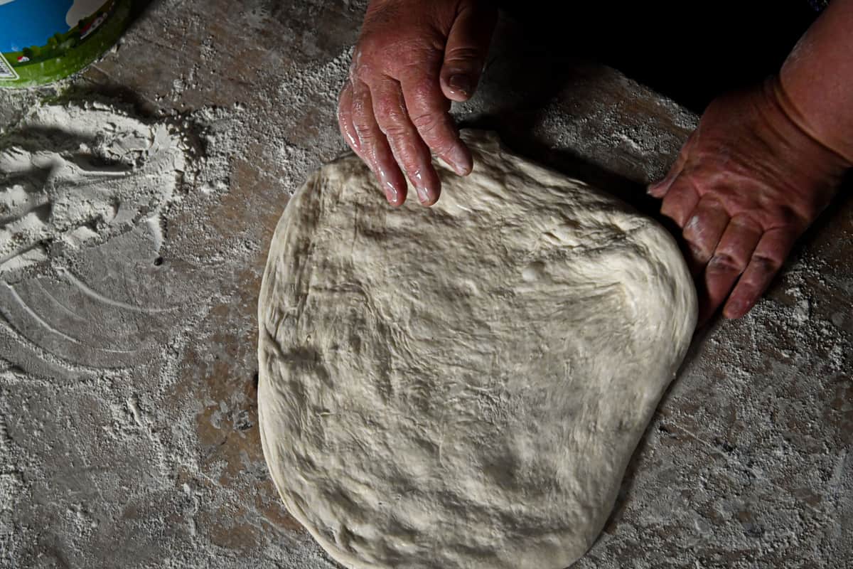 Hands kneading pizza dough on a floured surface