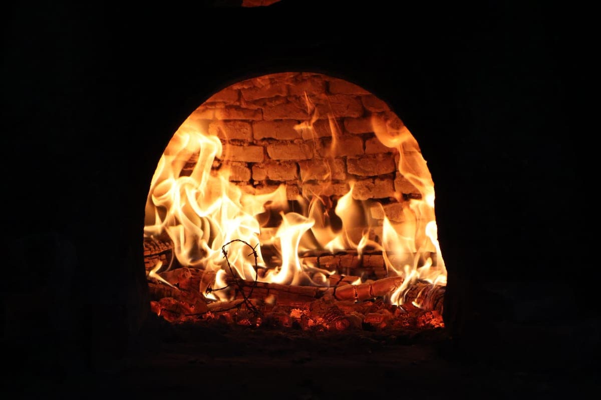 A wood-fired pizza oven with bright flames rolling across the dome